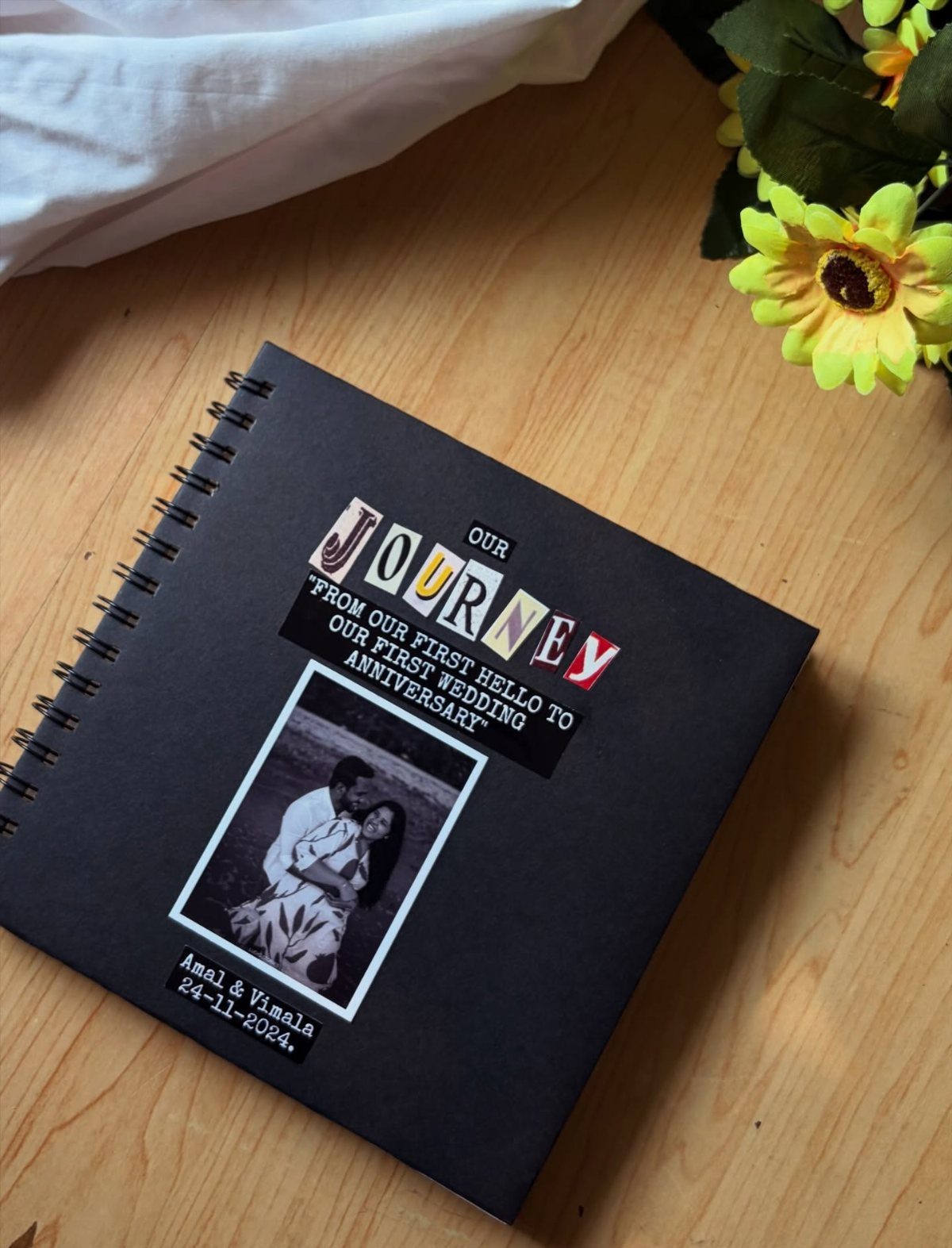 Black spiral journal with a couple's photo and anniversary text on wooden table