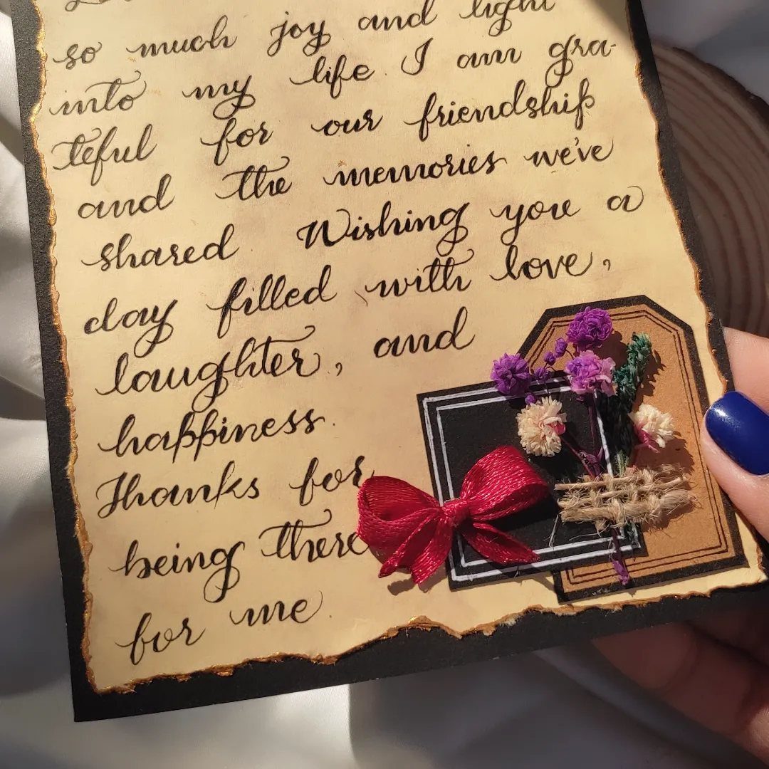 Handwritten letter on aged paper decorated with dried flowers and a red bow.