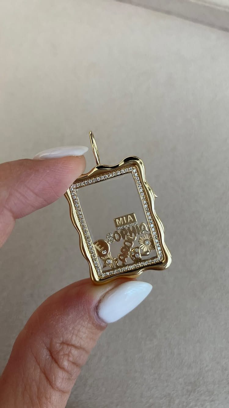 Gold rectangular pendant with custom name lettering held by fingers with white nails