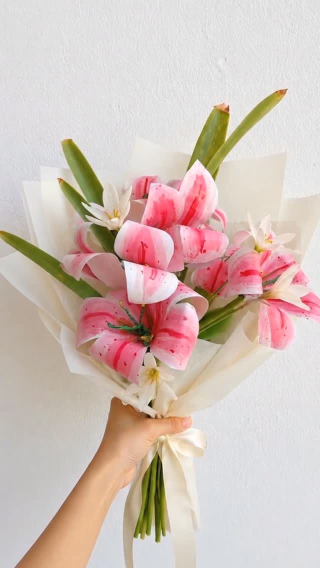 Bouquet of pink and white lilies wrapped in white paper held by a hand.