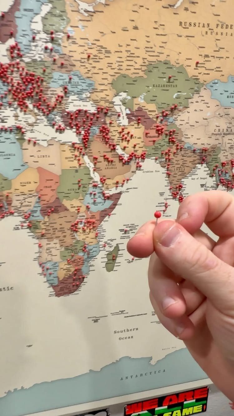 World map with red push pins and a hand adding another pin.