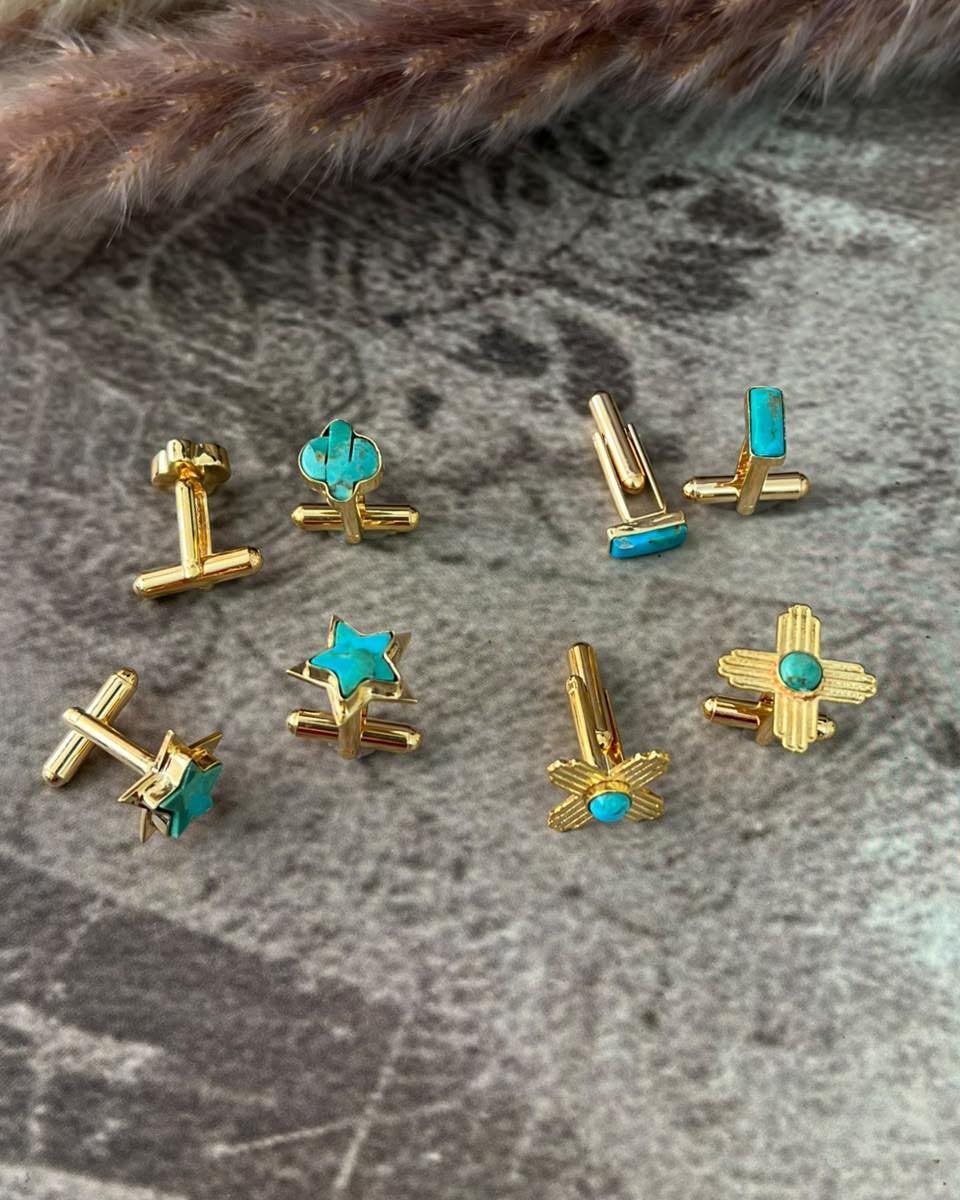 Gold cufflinks with turquoise stones arranged on a grey stone surface.