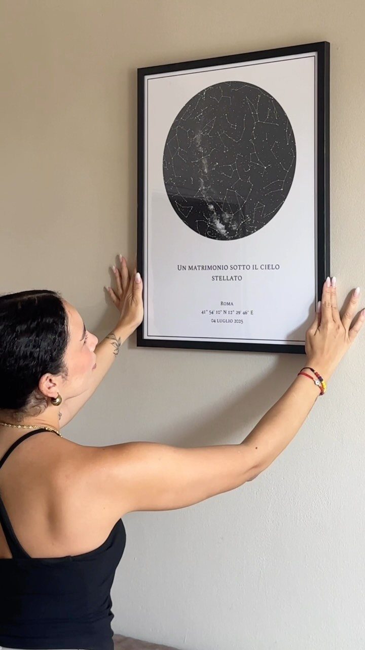 Woman hanging a framed custom star map with constellations on a beige wall.