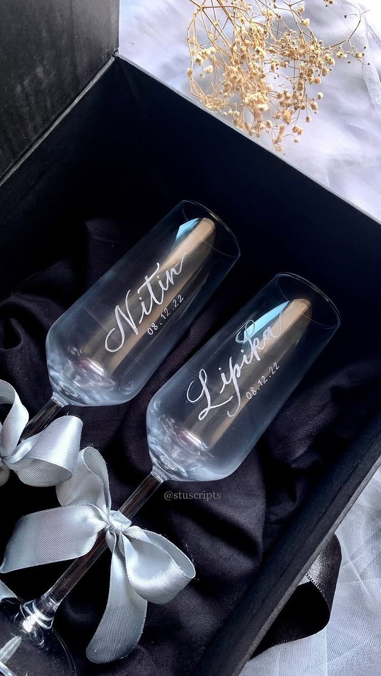 Two engraved champagne flutes in a black gift box with a white bow.