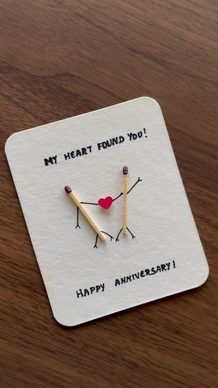 Anniversary card with matchstick figures holding a red heart on wooden background