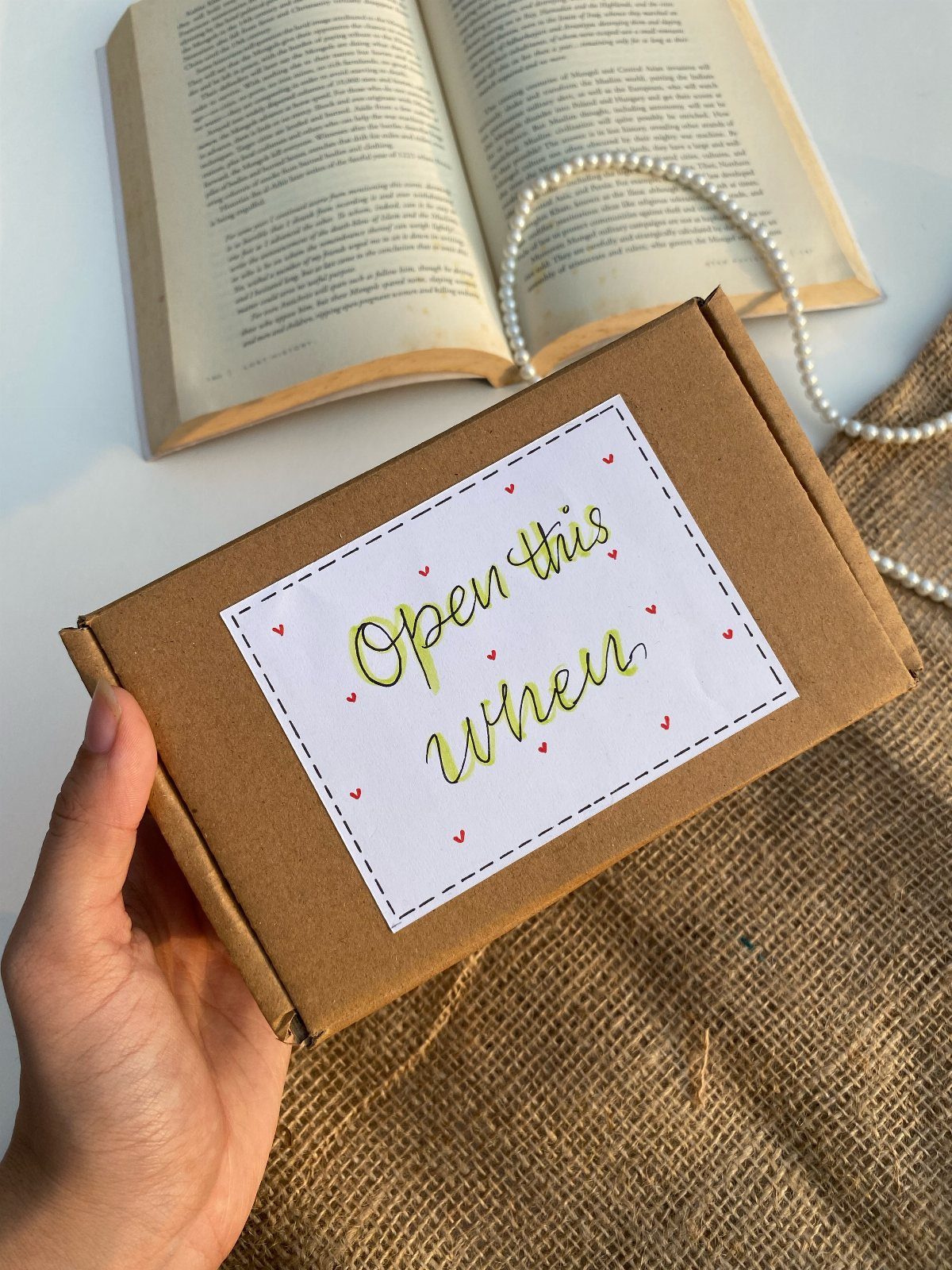 Brown cardboard gift box with Open this when label held by a hand.
