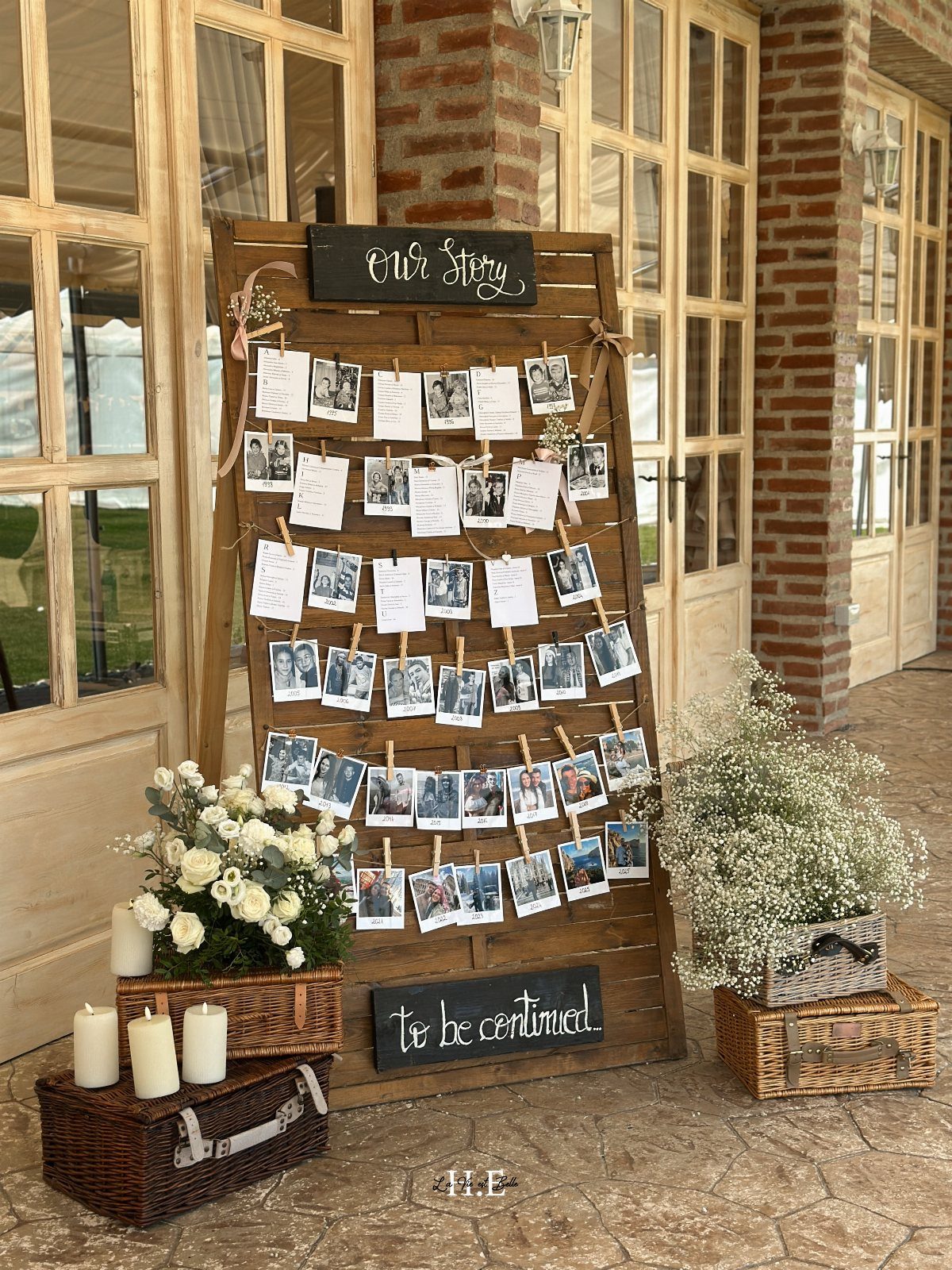 Wooden photo display board with polaroids, white flowers, and candles on stone floor