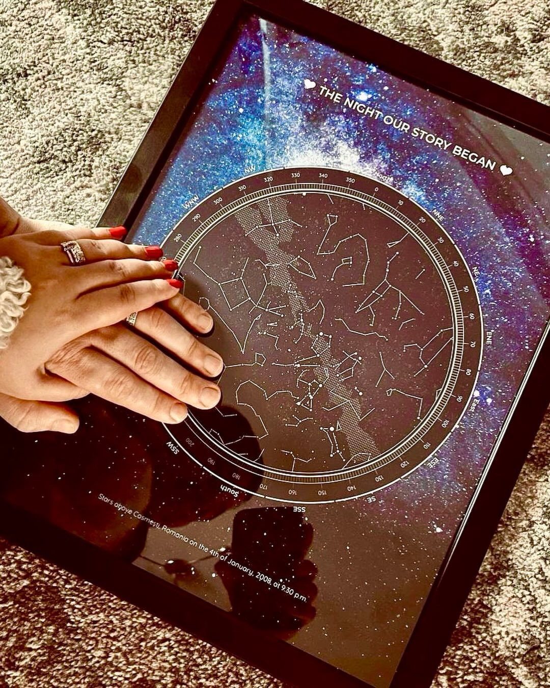 Framed custom star map with constellations and nebula background under two resting hands.