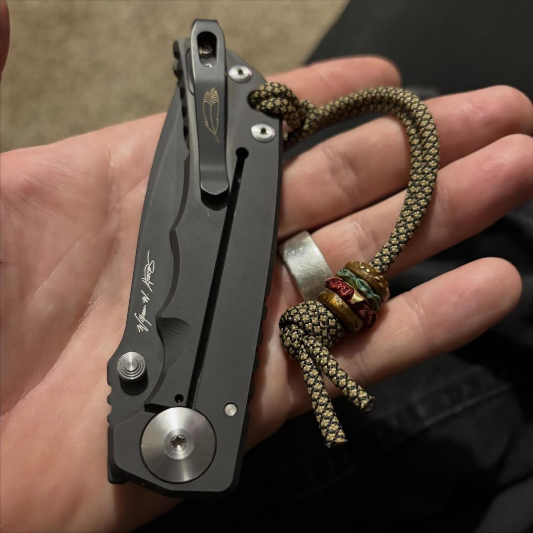 Black folding pocket knife with a braided paracord lanyard held in a hand.
