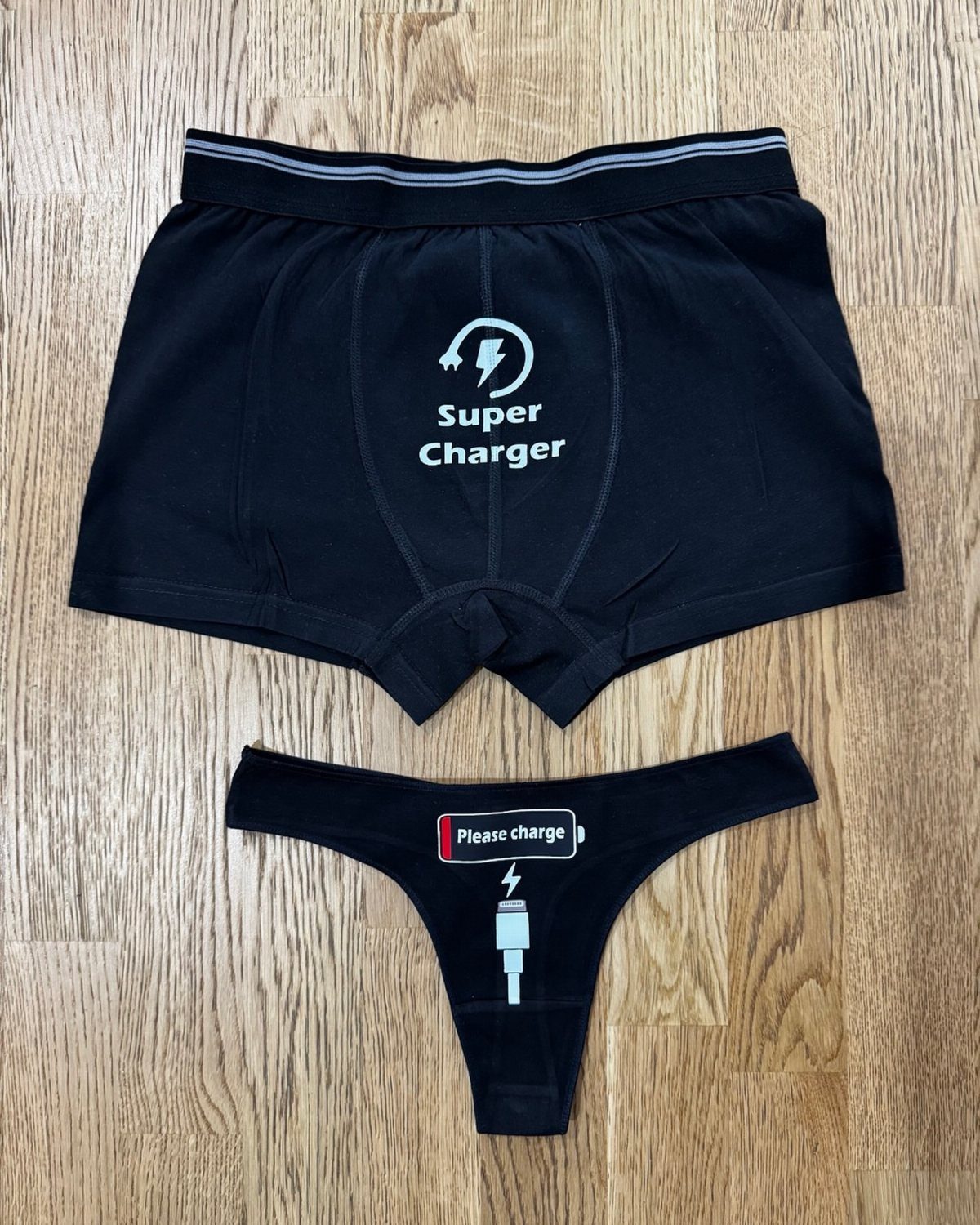 Matching black underwear set with charging battery puns on a wooden floor.