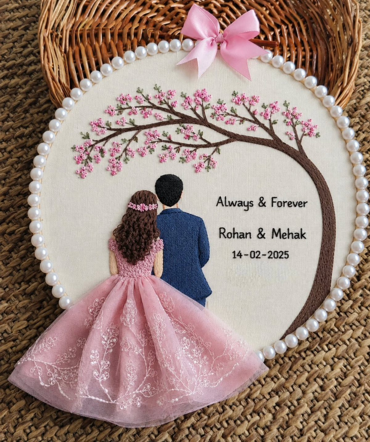 Embroidered circular portrait of a couple under a pink flowering tree with names.