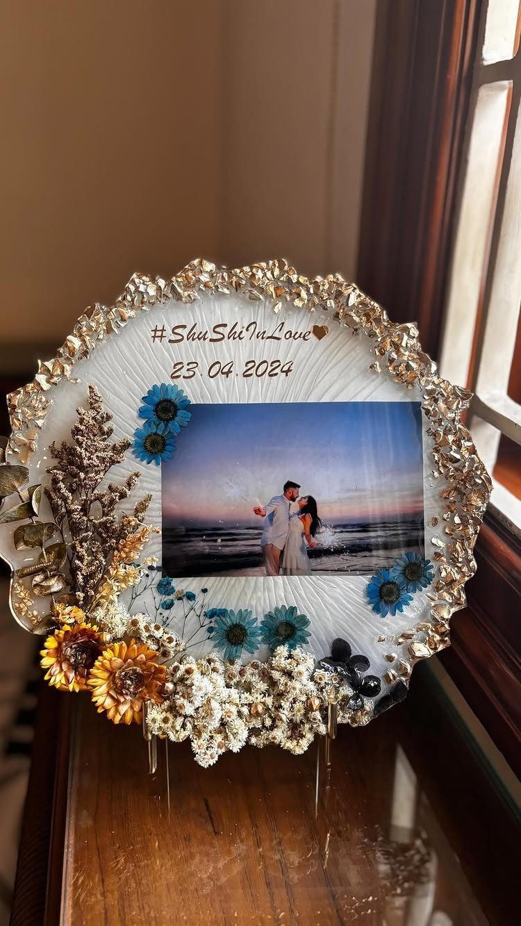 Circular resin art piece with a couple's beach photo and dried flowers.