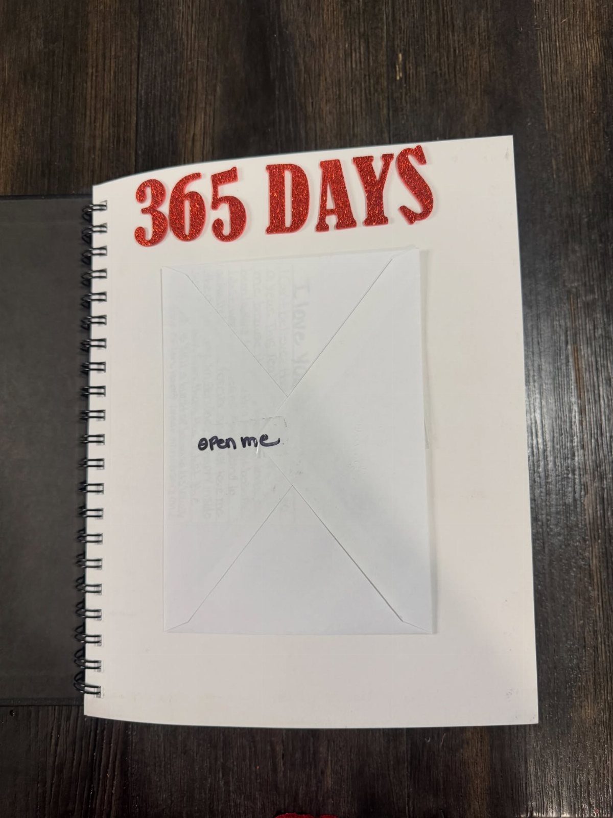 Spiral notebook with red glittery 365 DAYS text and a small white envelope.