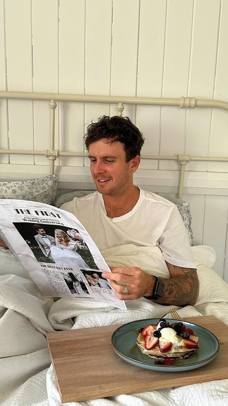 Man in bed reading a custom wedding newspaper with a breakfast tray nearby.