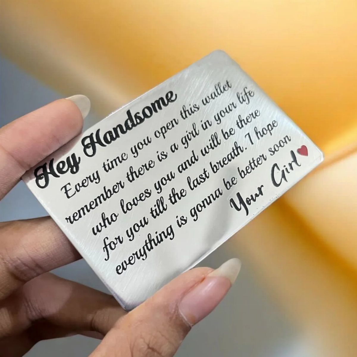 Silver metal wallet card with engraved romantic message held by a hand.