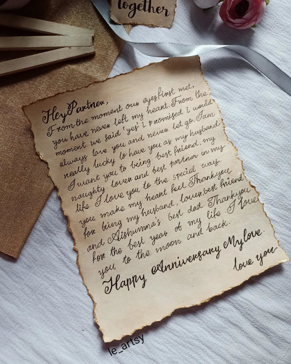 Handwritten love letter on aged parchment paper with burnt edges on white wood.