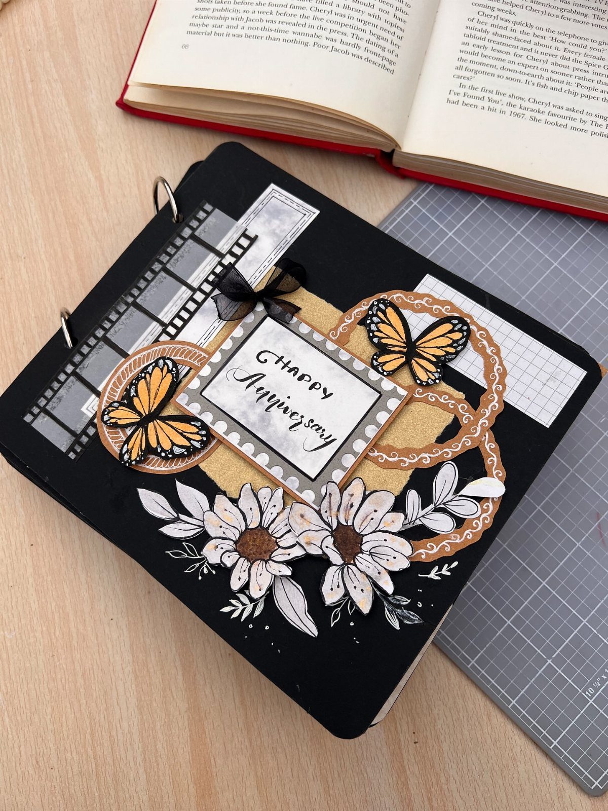 Black anniversary journal decorated with butterflies, white flowers, and a Happy Anniversary card.