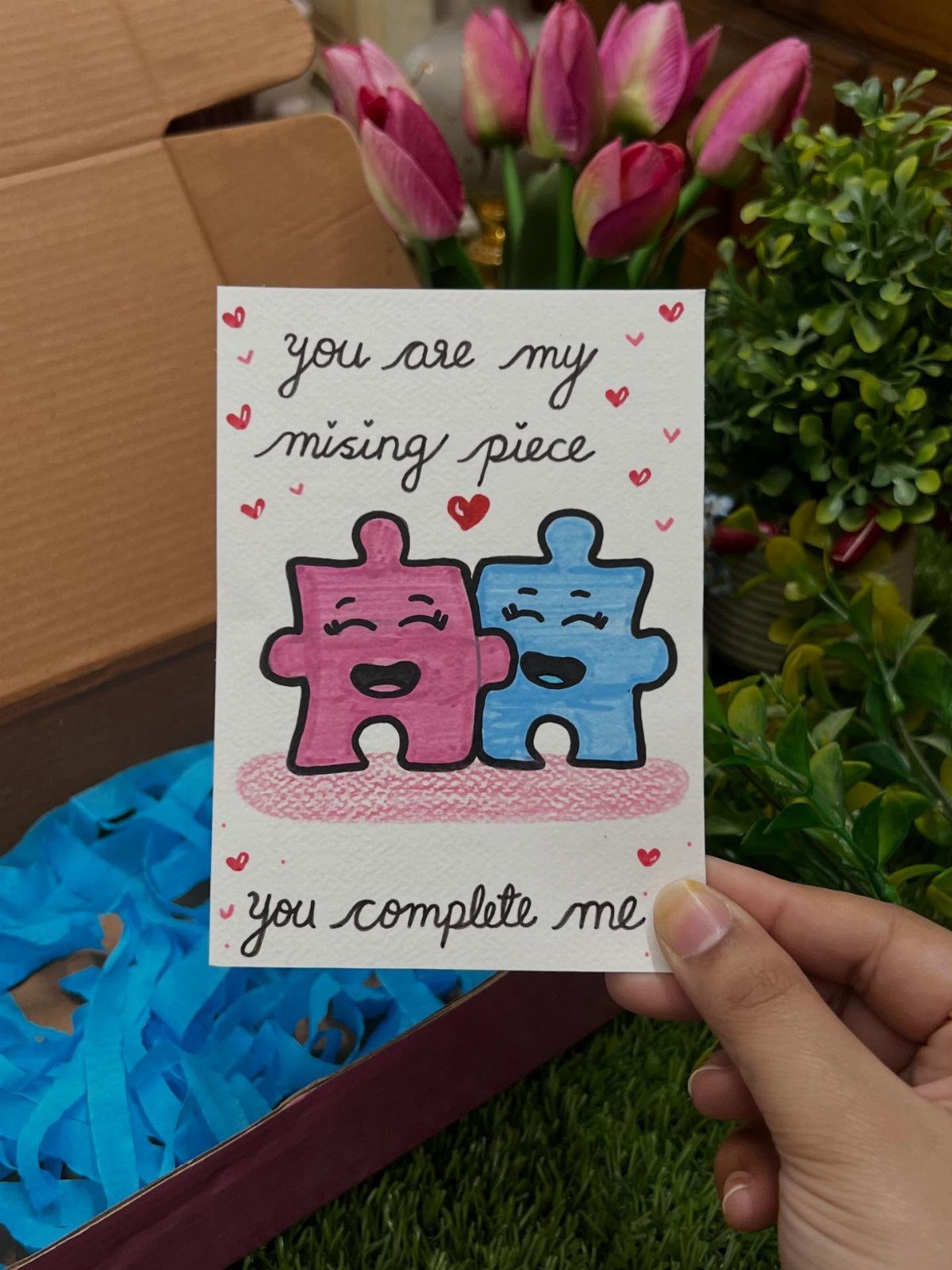 Handmade card with pink and blue puzzle pieces and romantic text held by hand.