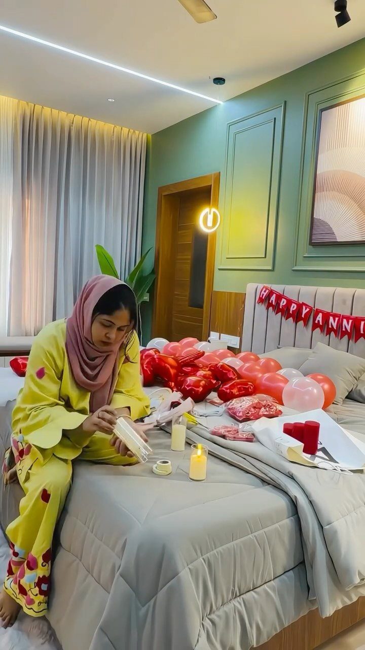Woman sitting on a bed decorated with balloons and anniversary banner for a celebration.