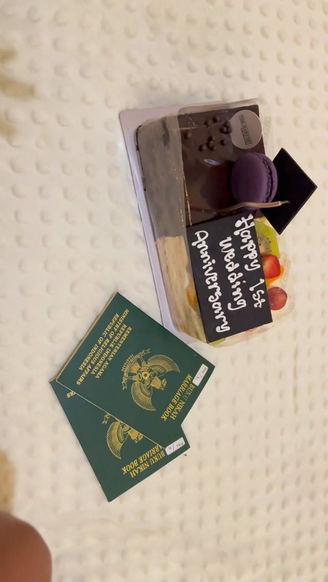 Anniversary cake with a 1st wedding anniversary sign and two green marriage books.