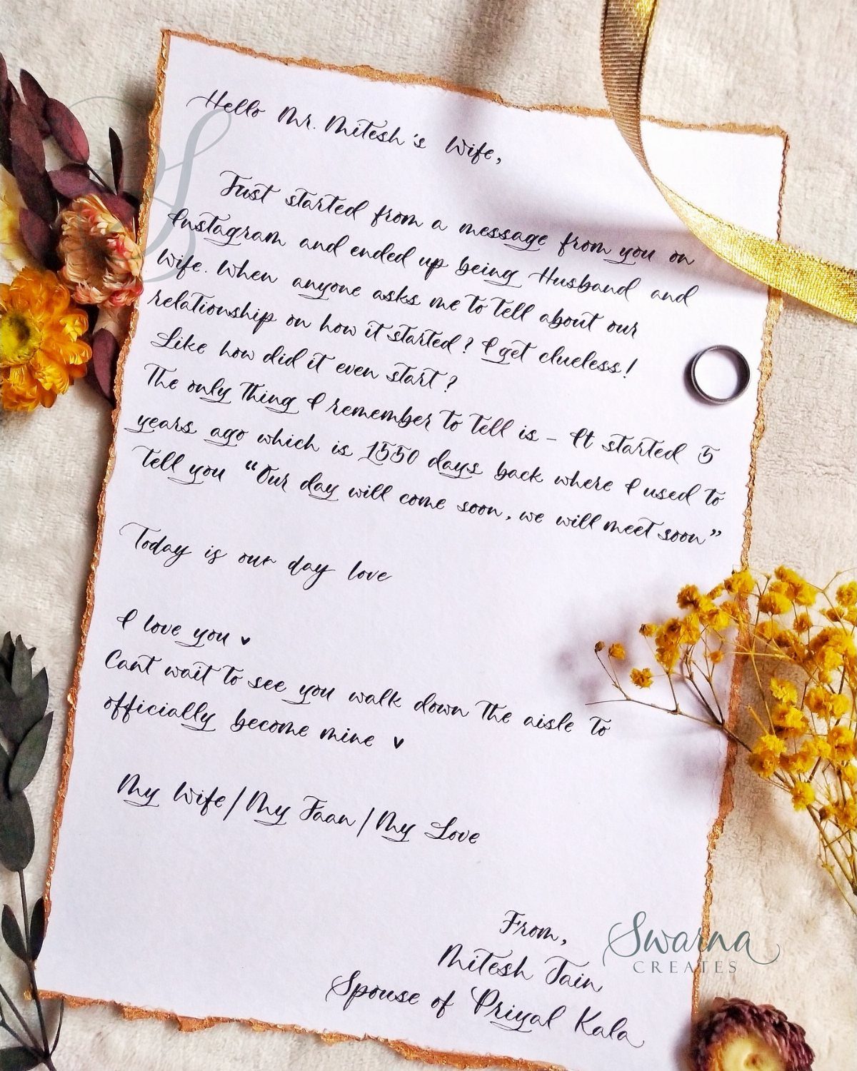 Handwritten love letter with gold edges surrounded by dried flowers and a ring.