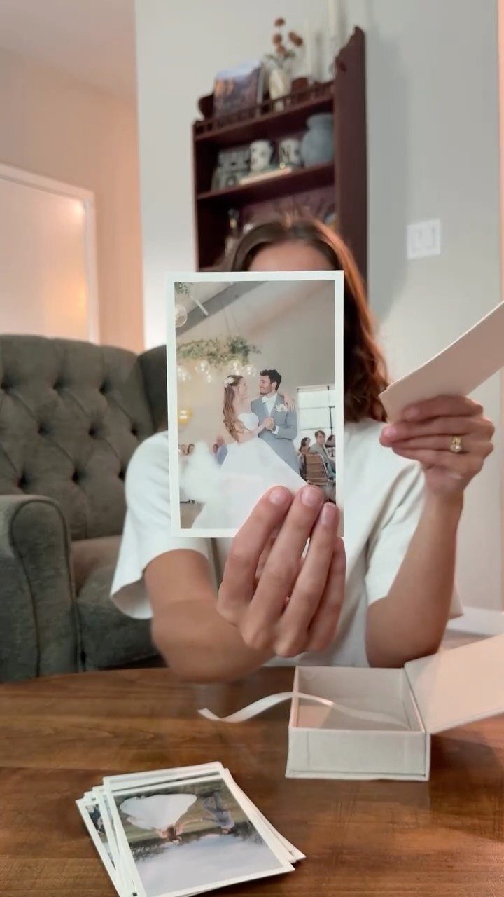 Woman holding a wedding photograph with more prints and a white box on table