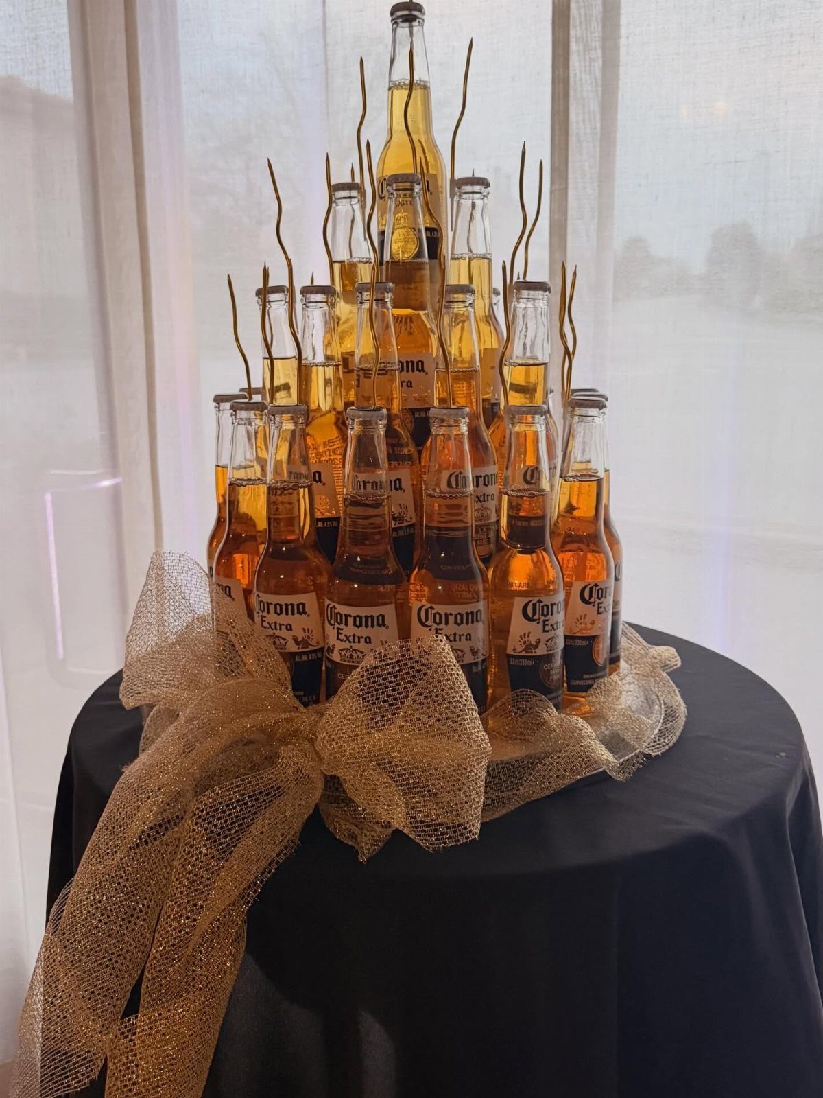 Pyramid of Corona beer bottles tied with a large gold mesh bow.