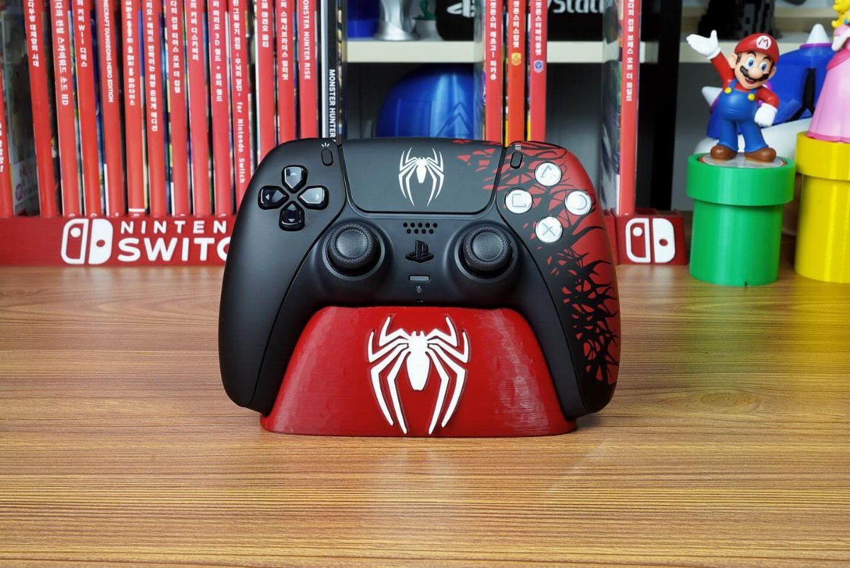 Spider-Man themed PlayStation controller on a red charging dock on a wooden desk