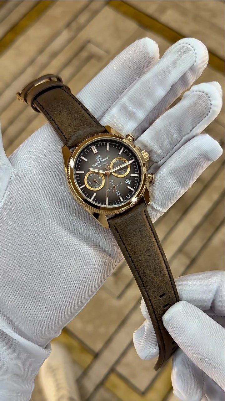 Gold chronograph watch with brown leather strap held by gloved hands.
