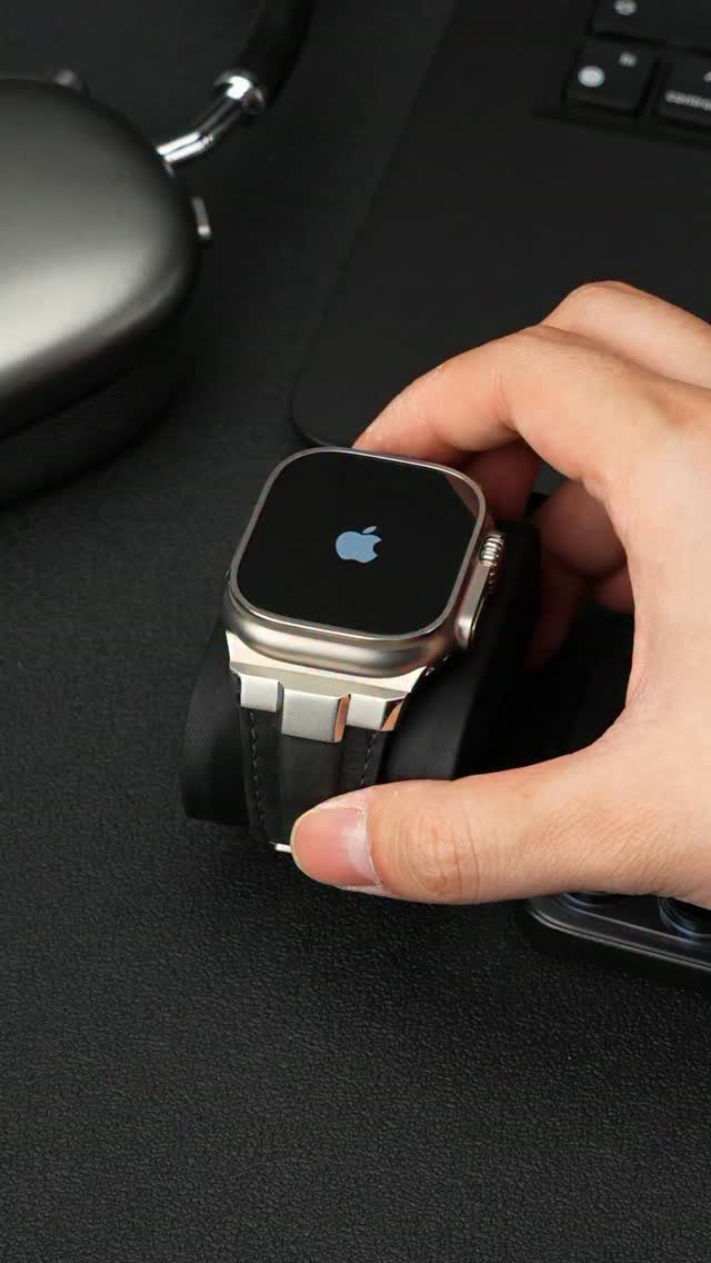 Silver Apple Watch with black leather strap held by a hand on desk