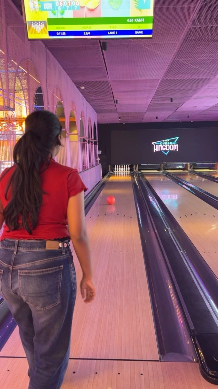 Woman in red shirt bowling in a purple-lit alley with a red ball.
