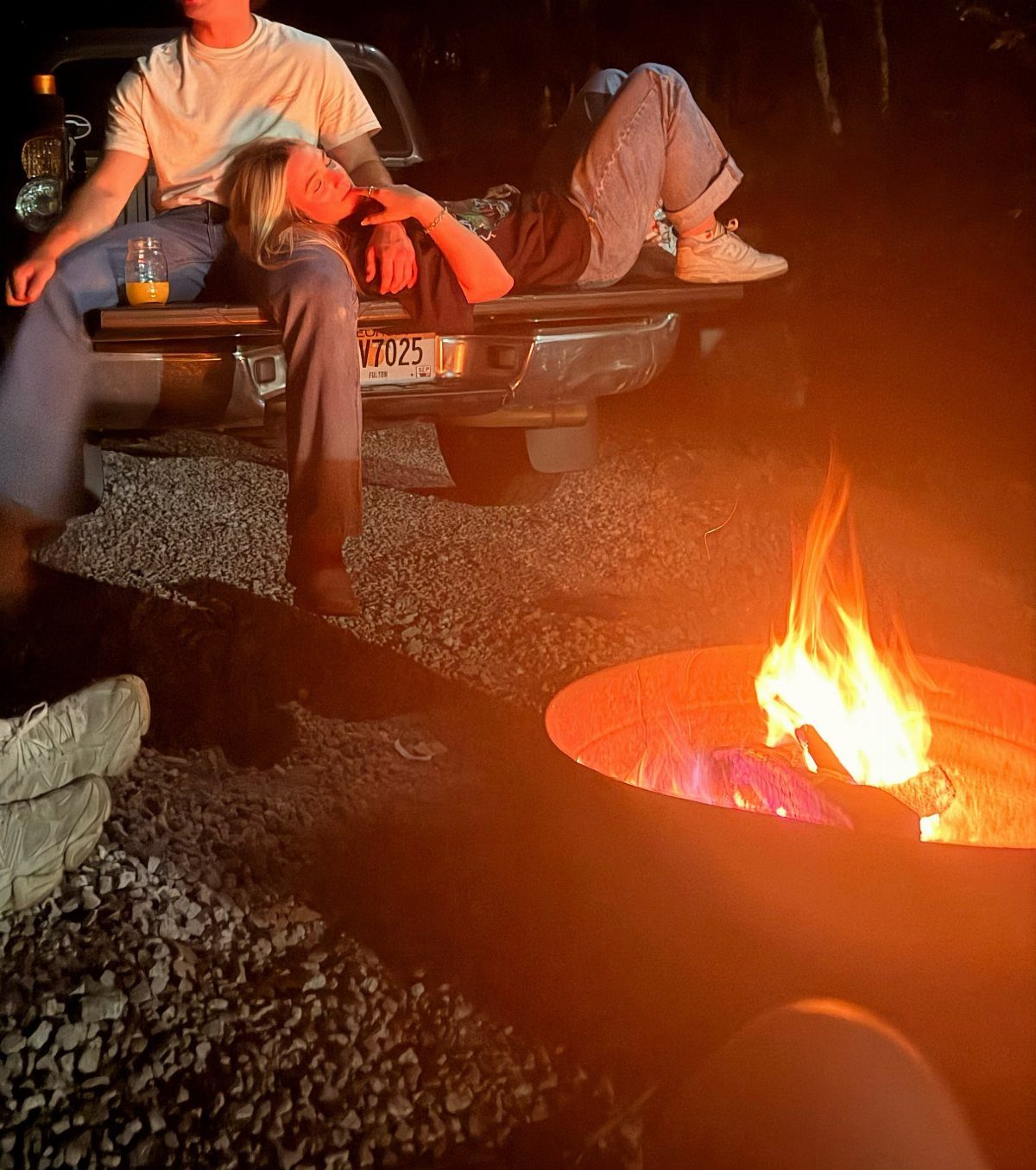 Couple relaxing in a pickup truck bed next to a glowing outdoor bonfire.