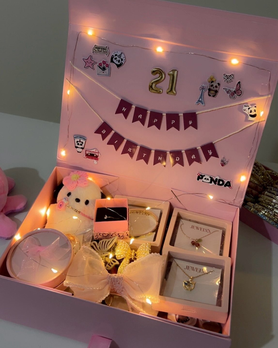 Pink birthday gift box with jewelry, plush toy, and 21st birthday decorations.