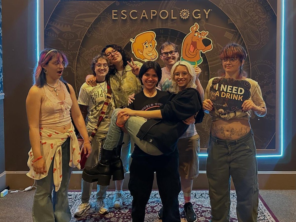 Six young women posing together at an escape room with a drink sign.