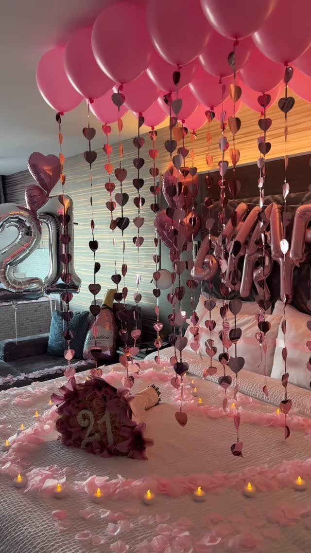 Romantic 21st birthday bedroom decoration with pink balloons, heart garlands, and rose petals.