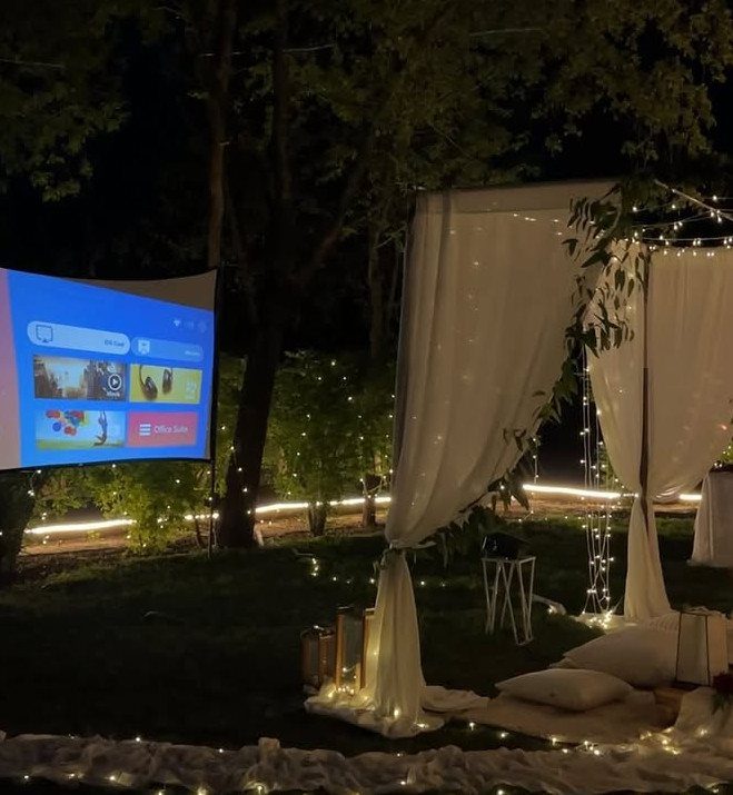 Outdoor movie night setup with a projector screen, white canopy, and fairy lights.