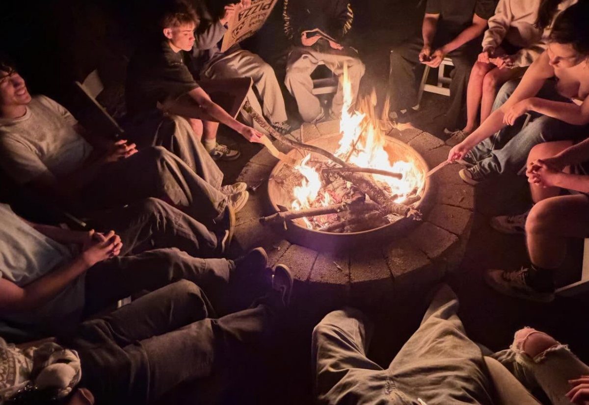 Young men roasting marshmallows over a stone fire pit at night outdoors.