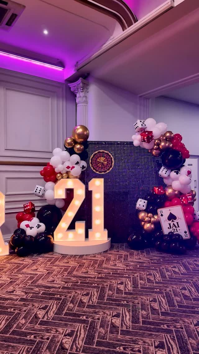 Illuminated number 21 surrounded by casino-themed balloons, giant dice, and playing cards.