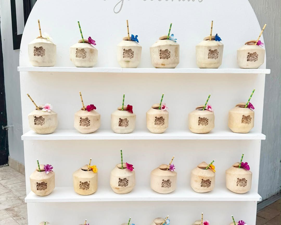 Carved coconut drink shells with straws and flowers on white display shelves.