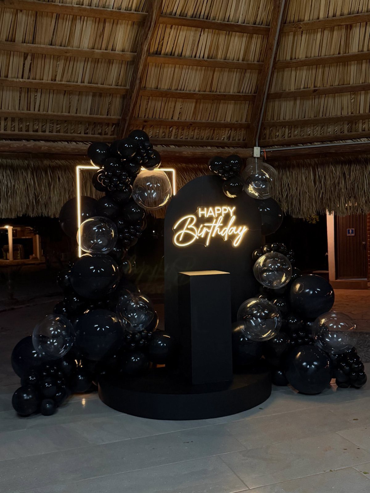 Black birthday party decoration with neon sign and black and clear balloons.