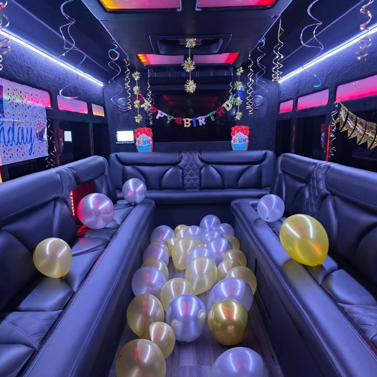 Party bus interior with black leather seats, neon lighting, and gold and silver balloons.