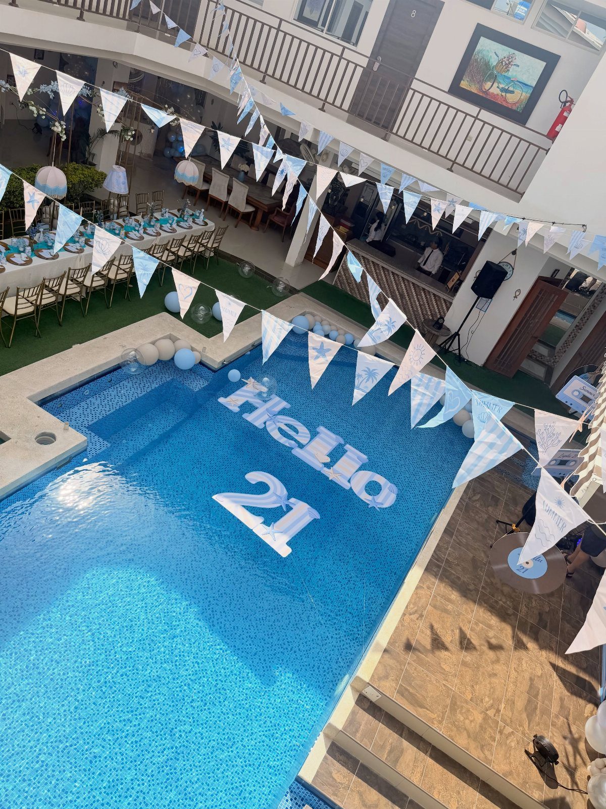 Swimming pool with Hello 21 float, blue bunting, and decorated dining table.