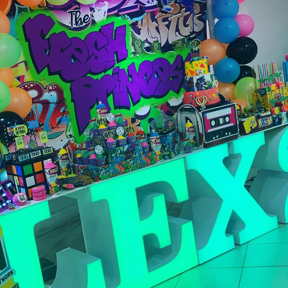 Colorful snack station with graffiti backdrop, boombox, and glowing teal letters for a party.