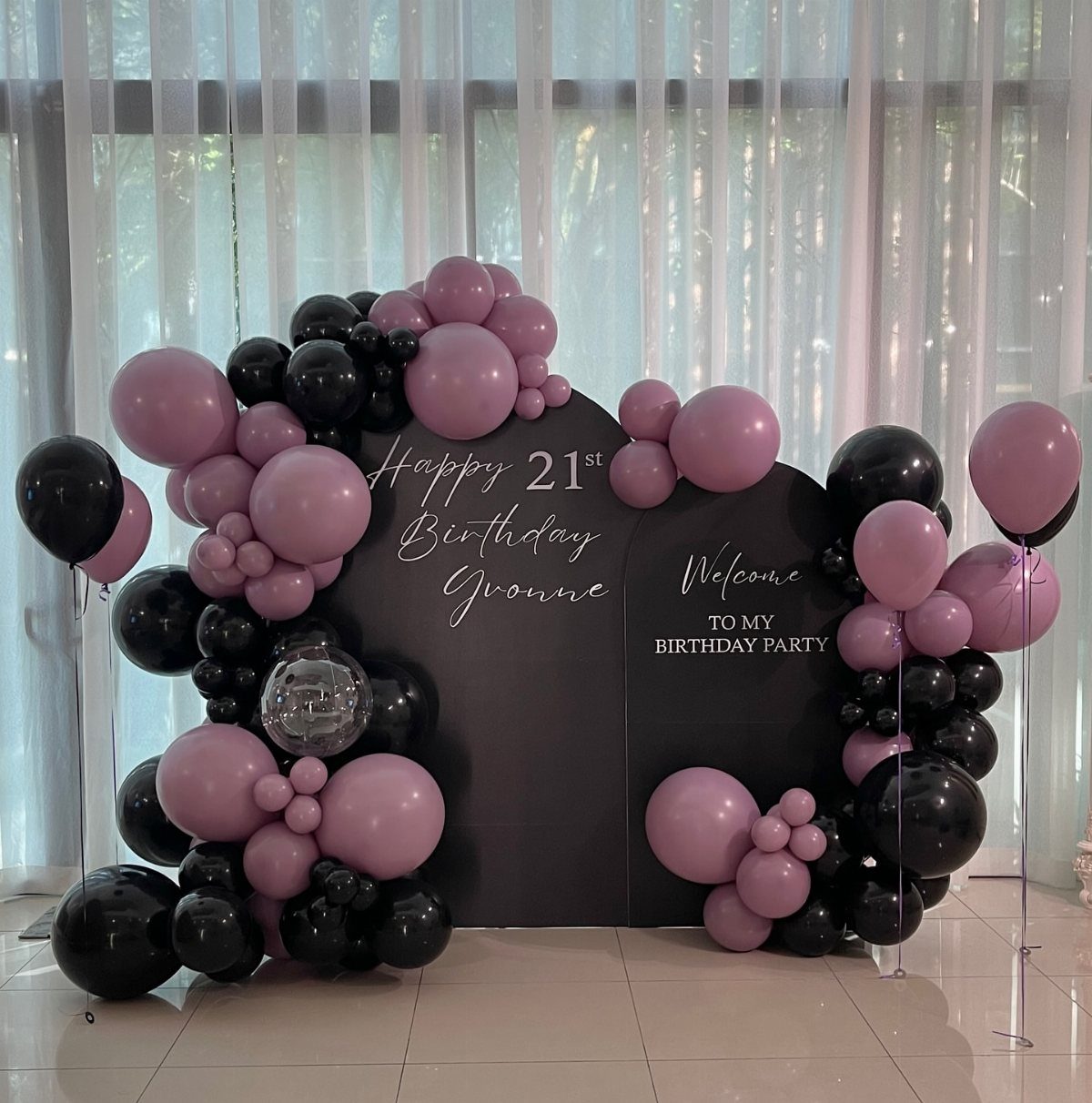 Black and pink balloon arch surrounding a 21st birthday party backdrop for Yvonne.