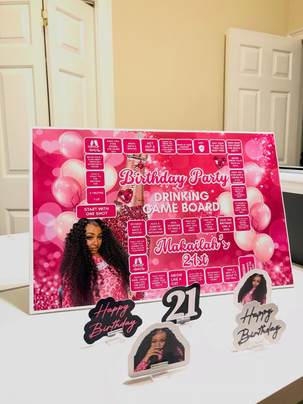 Pink 21st birthday drinking game board with a photo and celebratory acrylic signs.