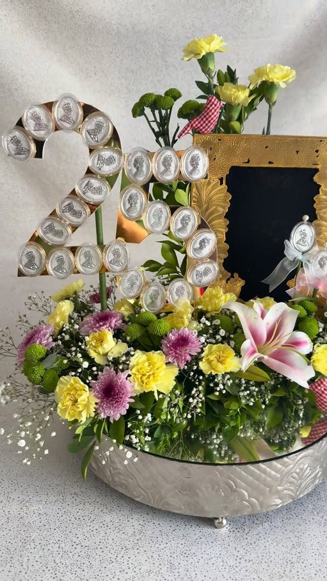 Floral arrangement in silver bowl with gold number 25 decorated with silver coins.