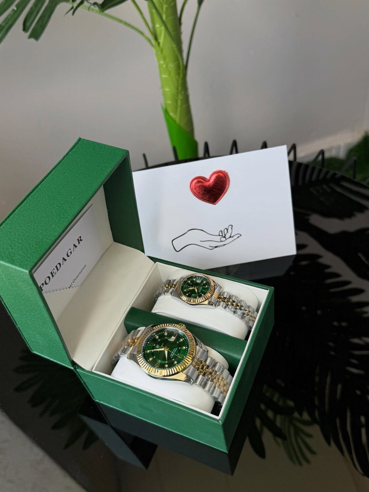 Two gold and silver watches with green faces in a green gift box.