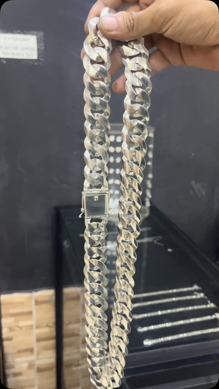 Silver curb link chain necklace held by a hand against a dark background