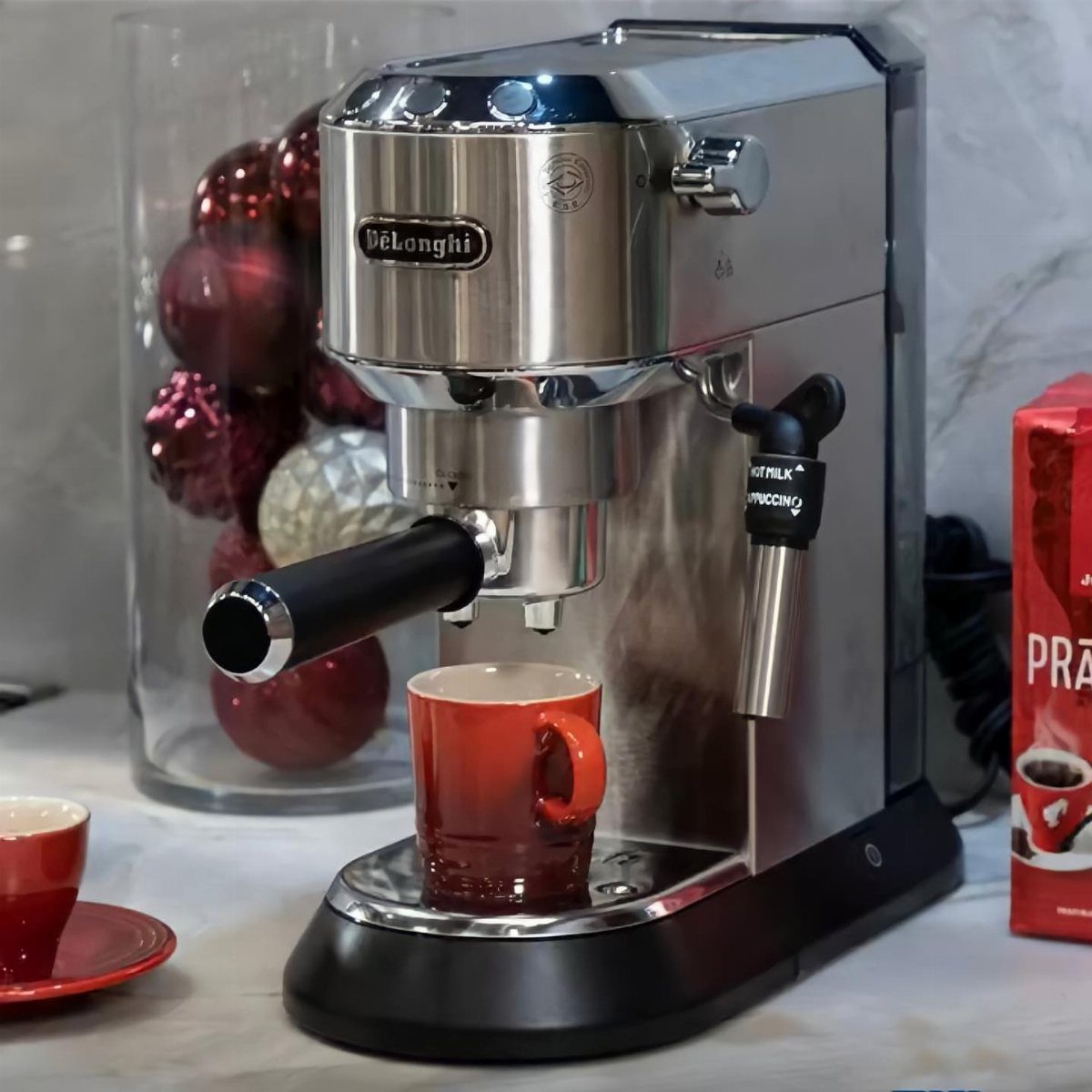 Silver espresso machine with a red coffee mug and Christmas ornaments in background