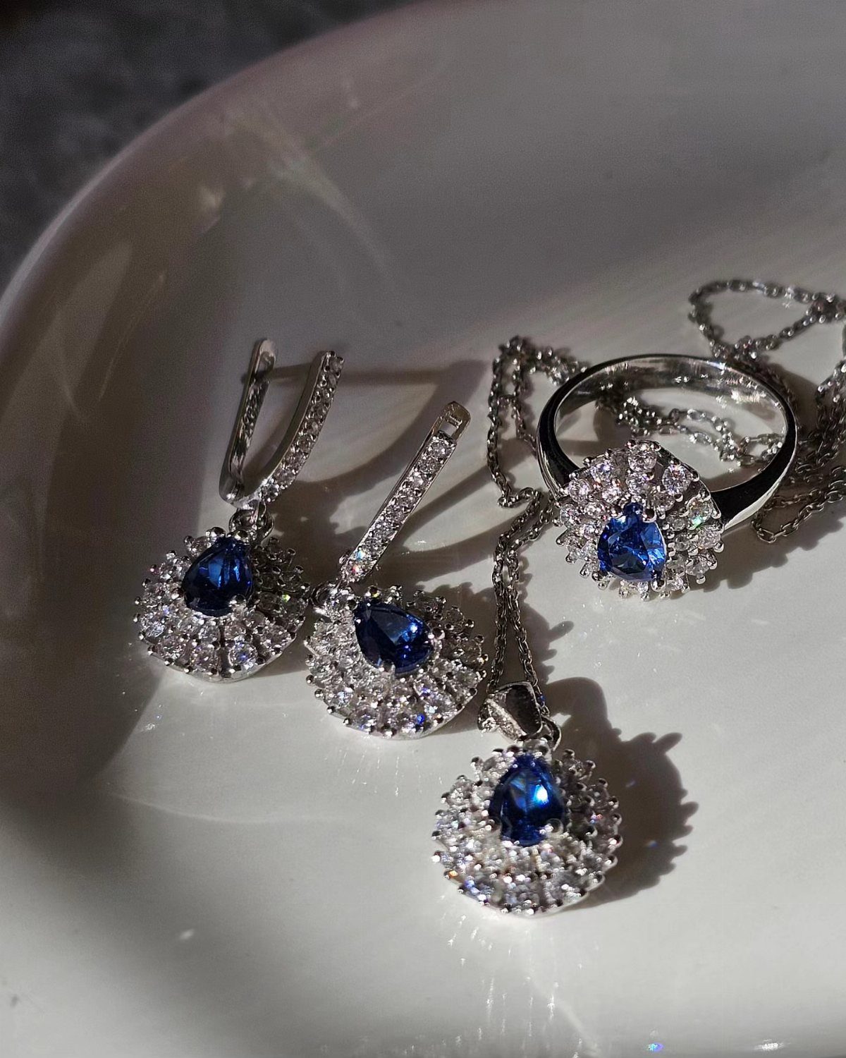 Silver jewelry set with blue teardrop gemstones including a ring, necklace, and earrings.